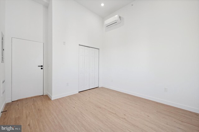 spare room with a high ceiling, light wood-type flooring, and a wall mounted air conditioner