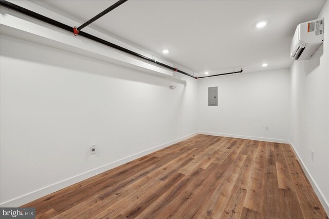 basement featuring hardwood / wood-style floors, an AC wall unit, and electric panel