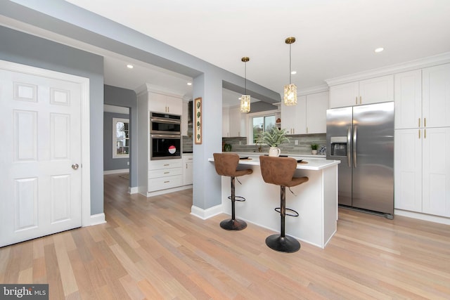 kitchen with decorative backsplash, a kitchen breakfast bar, stainless steel appliances, light hardwood / wood-style flooring, and white cabinets