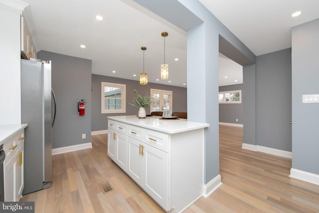 kitchen with white cabinets, light wood-type flooring, decorative light fixtures, and stainless steel refrigerator