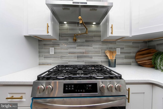 kitchen with light stone countertops, backsplash, gas range, extractor fan, and white cabinetry