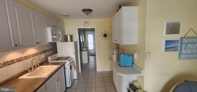 kitchen with sink, tasteful backsplash, light tile patterned flooring, white appliances, and white cabinets