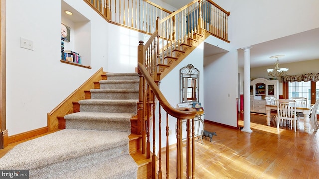 stairway featuring a notable chandelier, hardwood / wood-style flooring, a towering ceiling, and ornate columns