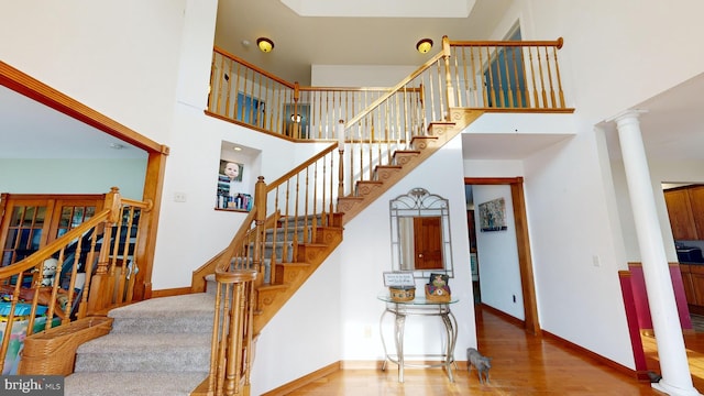 stairway featuring hardwood / wood-style flooring, decorative columns, and a high ceiling