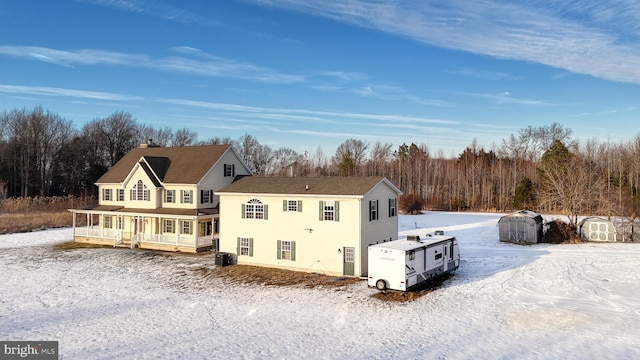 snow covered property with a sunroom, central AC unit, and a shed