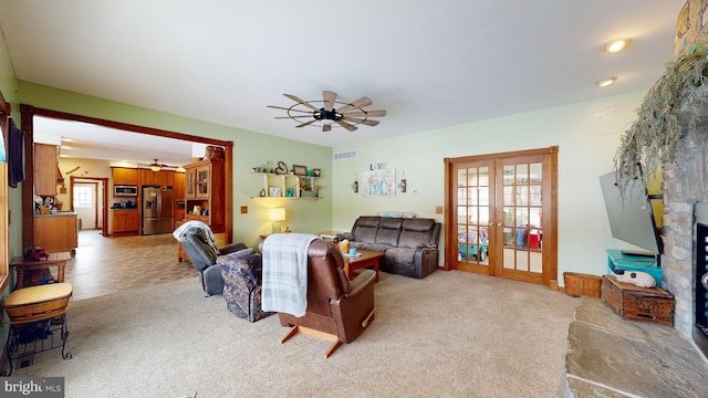 carpeted living room featuring french doors, ceiling fan, a stone fireplace, and a wealth of natural light