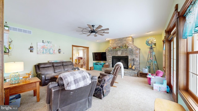 living room with light carpet, a stone fireplace, and ceiling fan