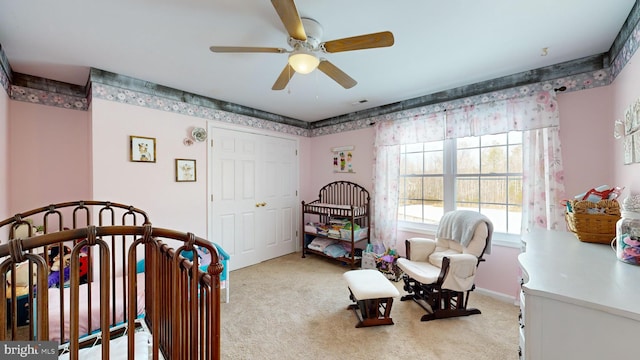 bedroom featuring a nursery area, light carpet, ceiling fan, and a closet