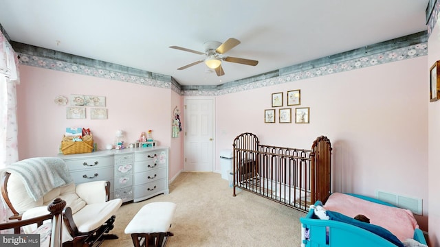 carpeted bedroom with a crib and ceiling fan