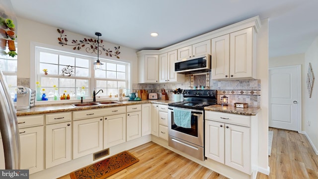 kitchen with tasteful backsplash, appliances with stainless steel finishes, sink, and light wood-type flooring