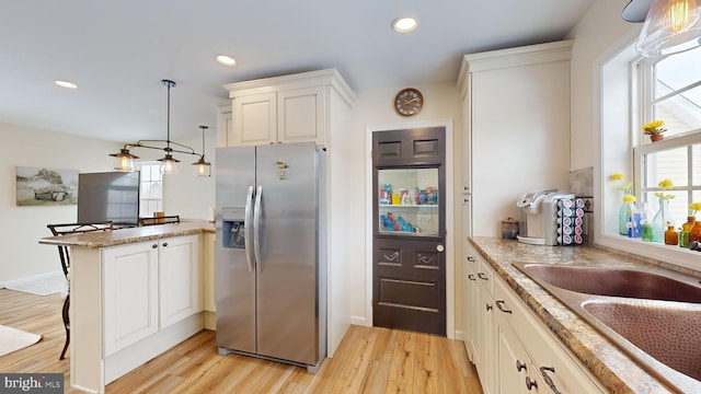 kitchen with stainless steel refrigerator with ice dispenser, a kitchen bar, hanging light fixtures, light wood-type flooring, and kitchen peninsula