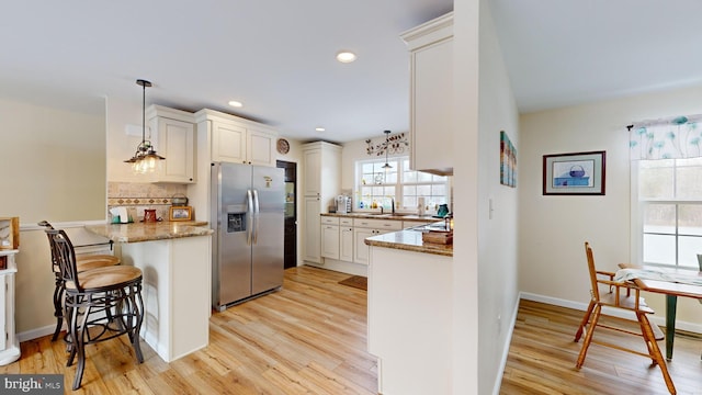 kitchen with a kitchen bar, stainless steel fridge with ice dispenser, hanging light fixtures, kitchen peninsula, and light hardwood / wood-style floors