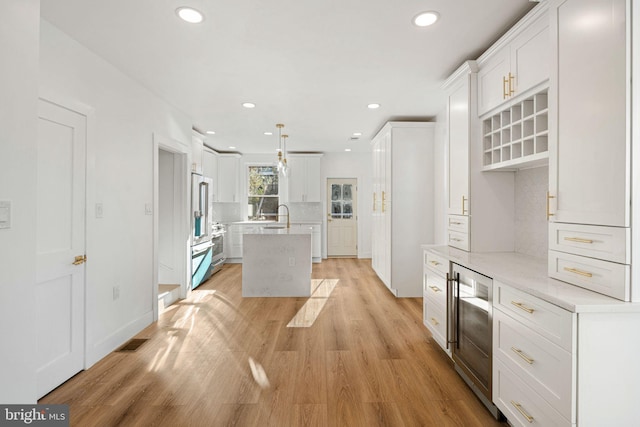 kitchen with a kitchen island with sink, sink, hanging light fixtures, light wood-type flooring, and white cabinetry