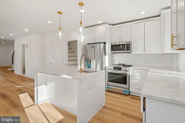 kitchen with pendant lighting, a center island with sink, white cabinets, light wood-type flooring, and appliances with stainless steel finishes