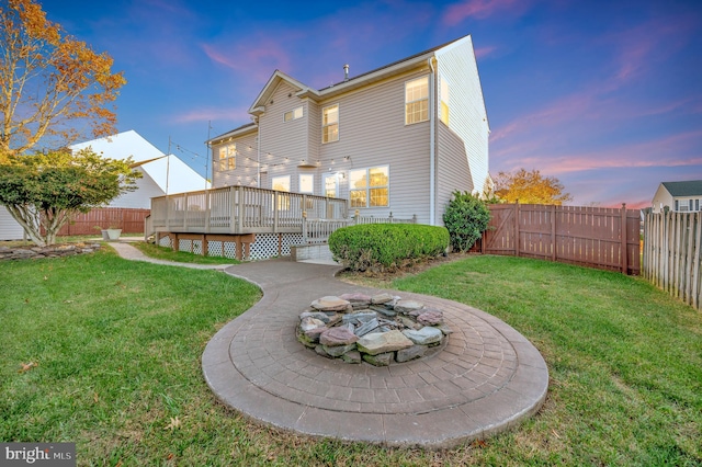 back house at dusk with a lawn, a wooden deck, and an outdoor fire pit