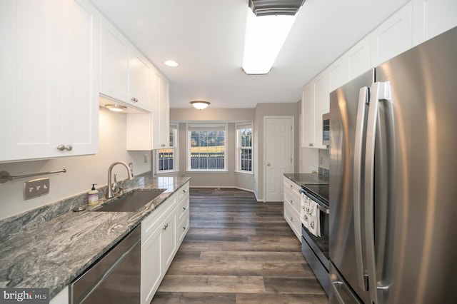 kitchen with dark stone counters, appliances with stainless steel finishes, sink, white cabinets, and dark wood-type flooring