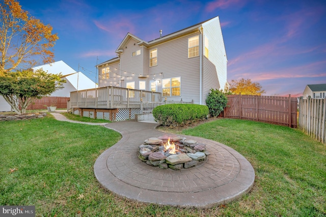 back house at dusk with a wooden deck, a fire pit, and a lawn