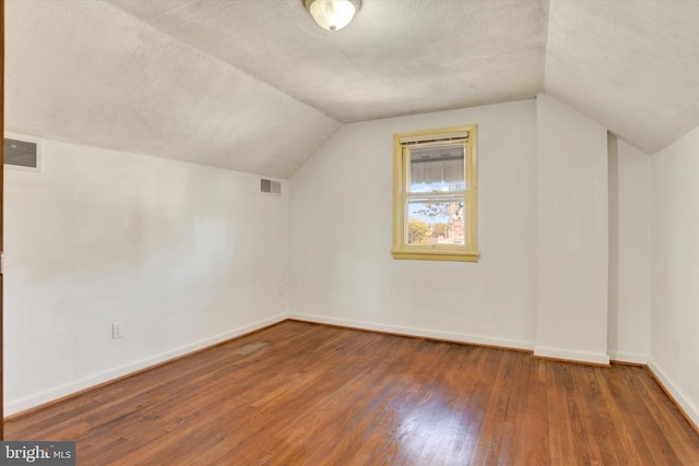 additional living space featuring vaulted ceiling, a textured ceiling, and dark hardwood / wood-style flooring