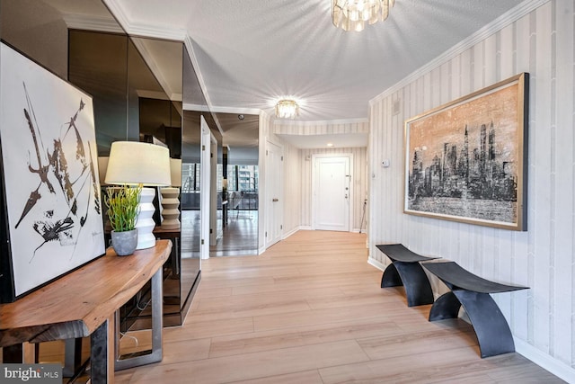 hall featuring ornamental molding, a chandelier, a textured ceiling, and light wood-type flooring