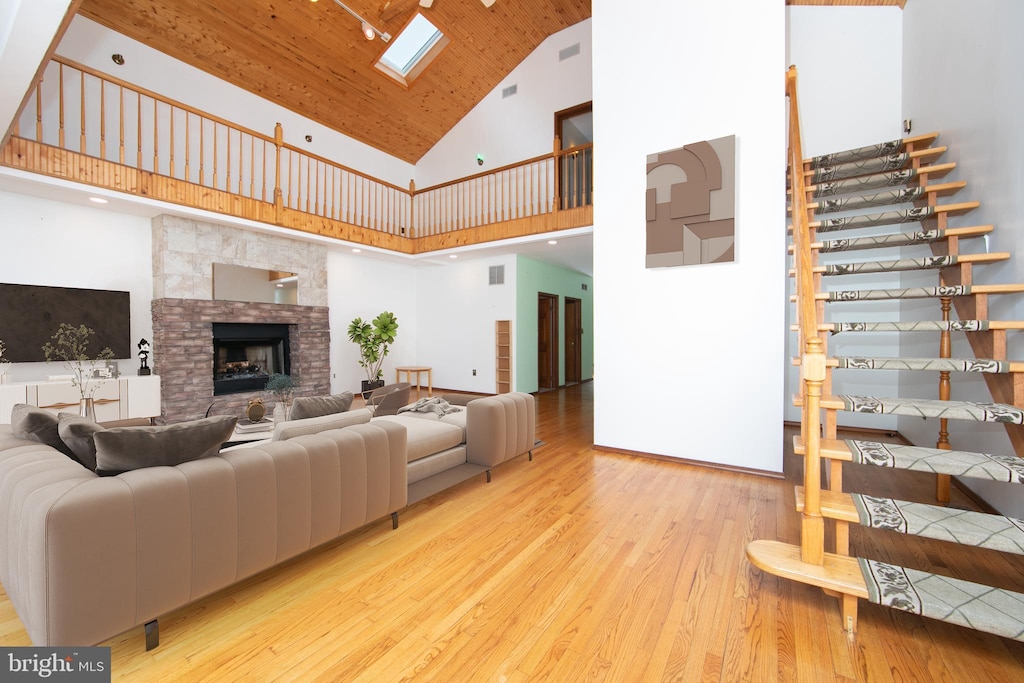 living room with a fireplace, light hardwood / wood-style flooring, high vaulted ceiling, and a skylight