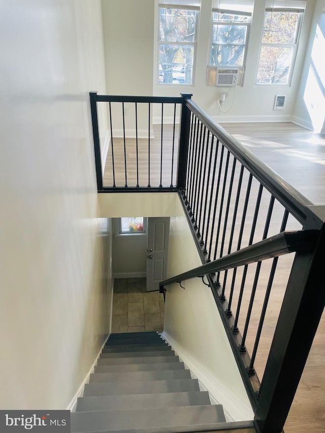 stairway featuring wood-type flooring, cooling unit, and a healthy amount of sunlight