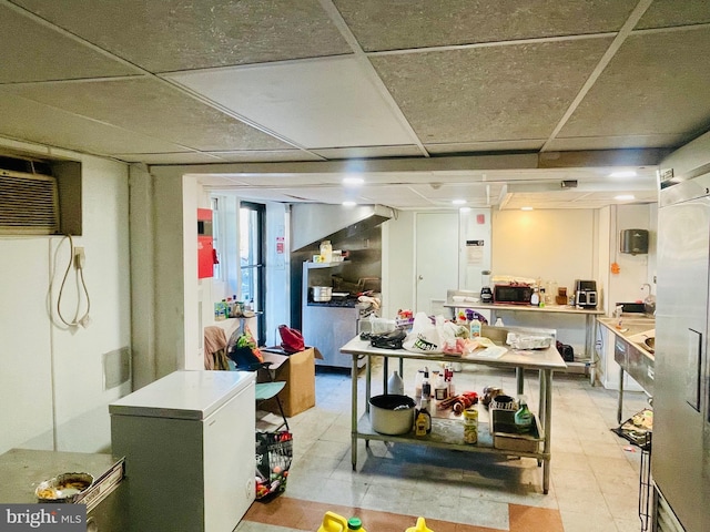 basement featuring a paneled ceiling, white refrigerator, and light tile patterned floors