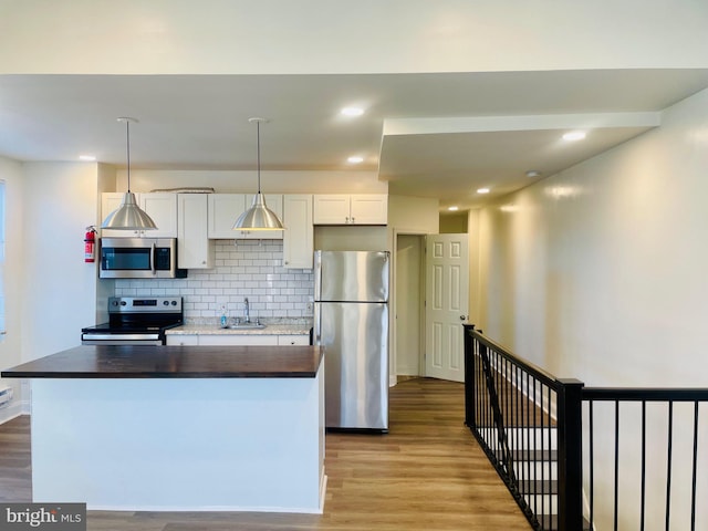 kitchen featuring appliances with stainless steel finishes, a center island with sink, decorative light fixtures, light hardwood / wood-style flooring, and white cabinetry