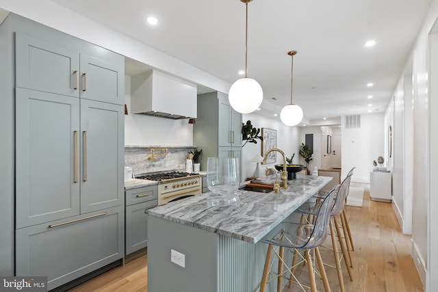 kitchen with a kitchen bar, high end stainless steel range oven, a large island with sink, pendant lighting, and light hardwood / wood-style flooring