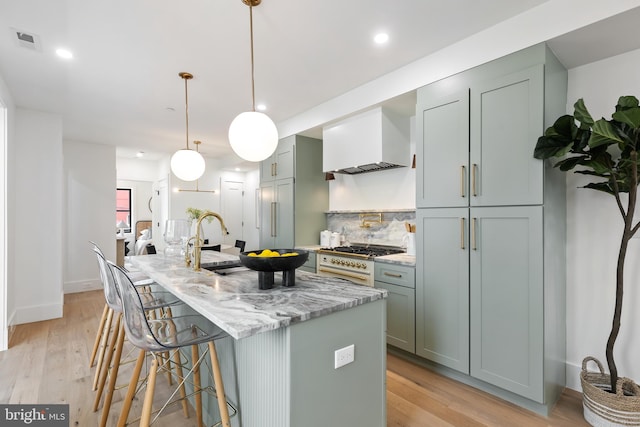 kitchen with light stone countertops, custom exhaust hood, a kitchen island with sink, high quality appliances, and hanging light fixtures