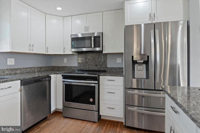 kitchen with light hardwood / wood-style flooring, appliances with stainless steel finishes, dark stone countertops, backsplash, and white cabinets