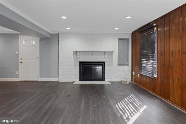 unfurnished living room featuring wood walls, dark hardwood / wood-style flooring, ornamental molding, electric panel, and a brick fireplace