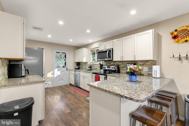 kitchen with white cabinetry, dark wood-type flooring, backsplash, kitchen peninsula, and appliances with stainless steel finishes