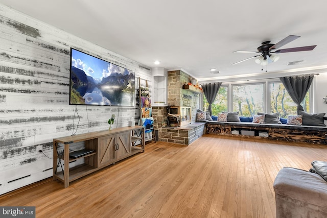 living room with ceiling fan, wood walls, and light wood-type flooring