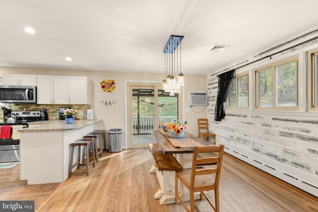 dining space with a wall unit AC, plenty of natural light, an inviting chandelier, and light hardwood / wood-style flooring