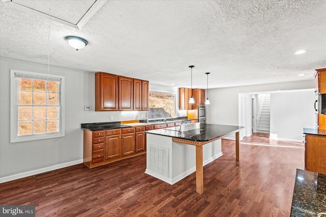 kitchen with a kitchen breakfast bar, a textured ceiling, pendant lighting, a center island, and dark hardwood / wood-style floors