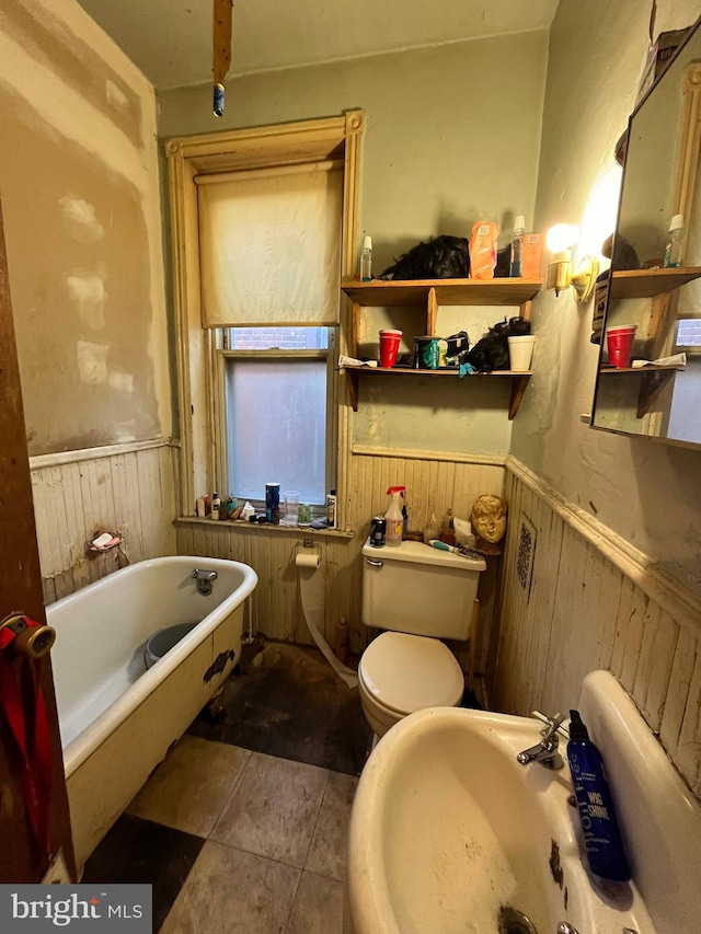 bathroom featuring toilet, wooden walls, sink, and a bathing tub