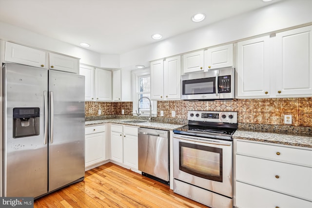 kitchen with sink, light hardwood / wood-style flooring, light stone countertops, white cabinetry, and stainless steel appliances