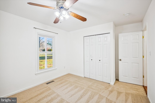 unfurnished bedroom with a closet, light colored carpet, and ceiling fan