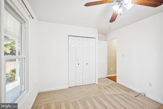 unfurnished bedroom with light carpet, a closet, multiple windows, and ceiling fan