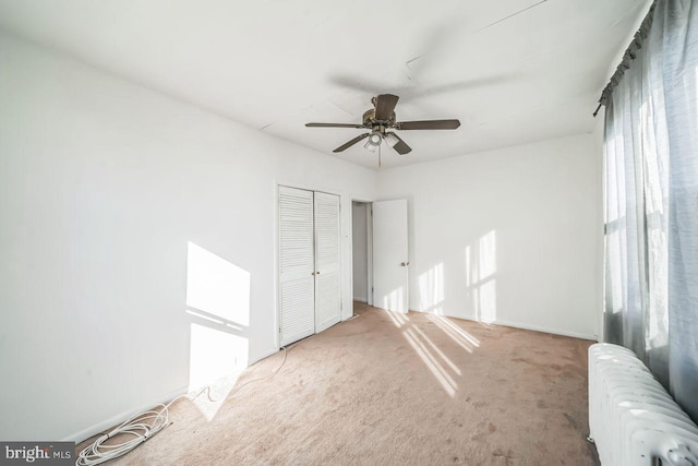 unfurnished bedroom featuring light carpet, a closet, radiator, and ceiling fan