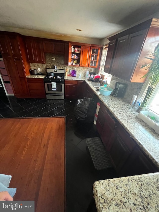 kitchen featuring sink, light stone counters, stainless steel gas range, and backsplash