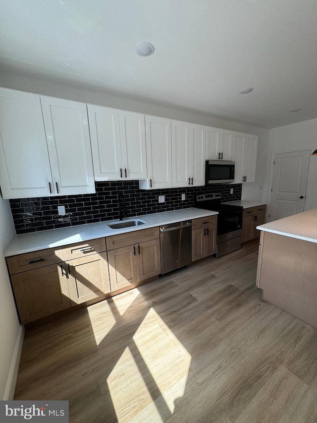 kitchen featuring stainless steel appliances, white cabinetry, decorative backsplash, sink, and light hardwood / wood-style floors