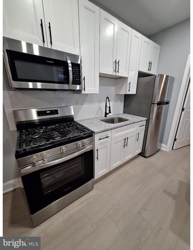 kitchen with white cabinets, light hardwood / wood-style floors, sink, and appliances with stainless steel finishes