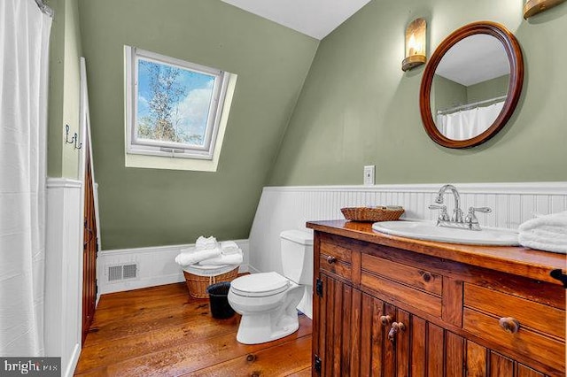 bathroom with toilet, hardwood / wood-style floors, vanity, and lofted ceiling with skylight