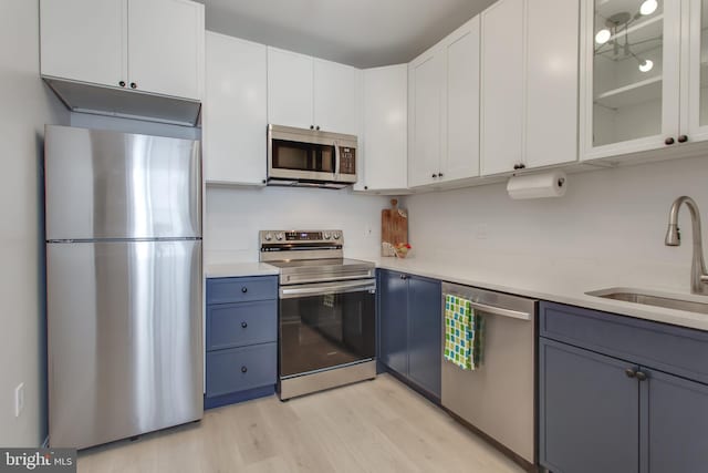 kitchen with stainless steel appliances, sink, blue cabinetry, light hardwood / wood-style floors, and white cabinetry