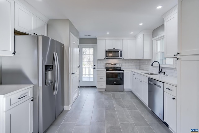 kitchen with stainless steel appliances, white cabinetry, sink, and backsplash