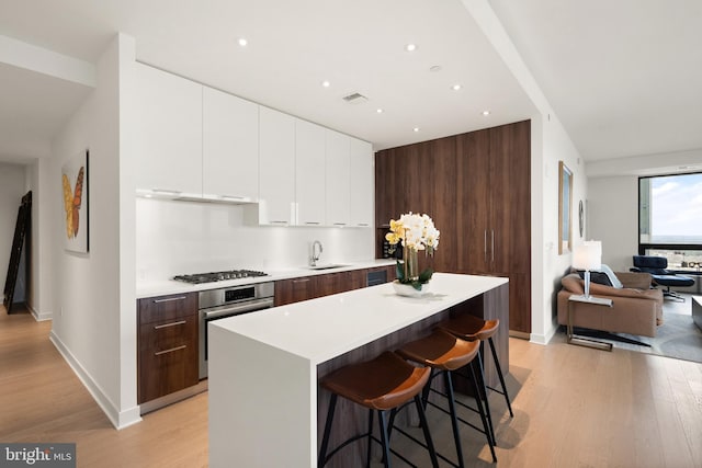 kitchen with light wood-type flooring, a breakfast bar, stainless steel appliances, sink, and white cabinetry