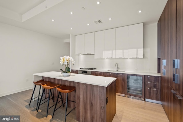 kitchen featuring beverage cooler, light hardwood / wood-style flooring, white cabinetry, sink, and a center island