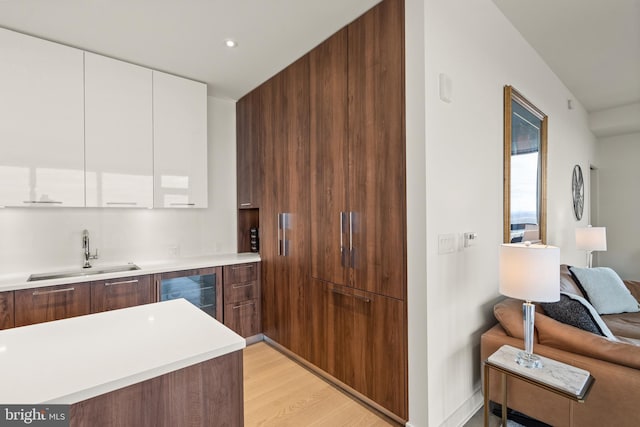 kitchen with white cabinets, light wood-type flooring, beverage cooler, and sink