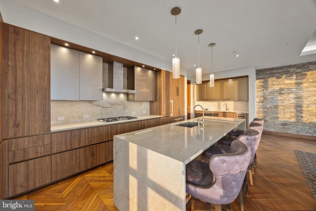 kitchen with dark parquet flooring, sink, wall chimney range hood, stainless steel gas cooktop, and pendant lighting